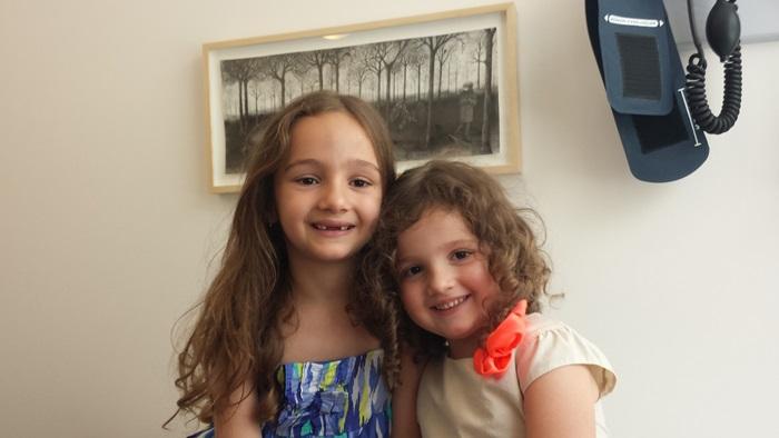 Two girls smile while sitting in an exam room